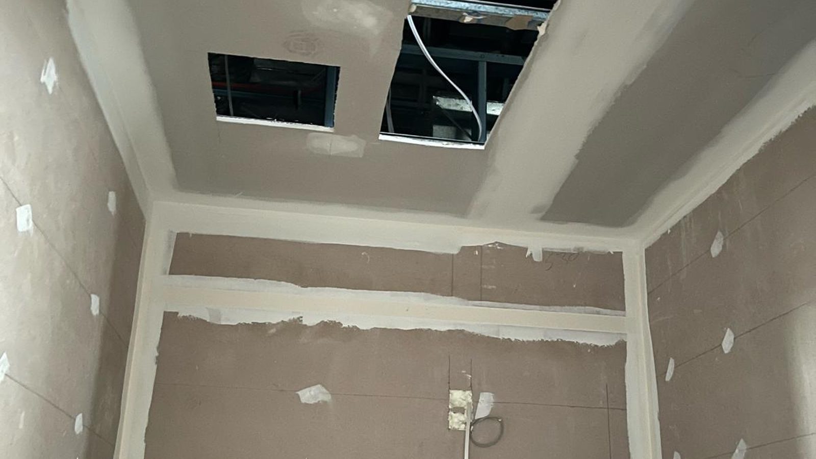 Bathroom ceiling set with the openings for services cut in above a lined wall
