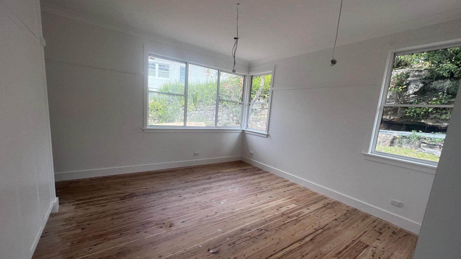 Bedroom with the walls and ceiling set around corner windows and the floorboards sanded below