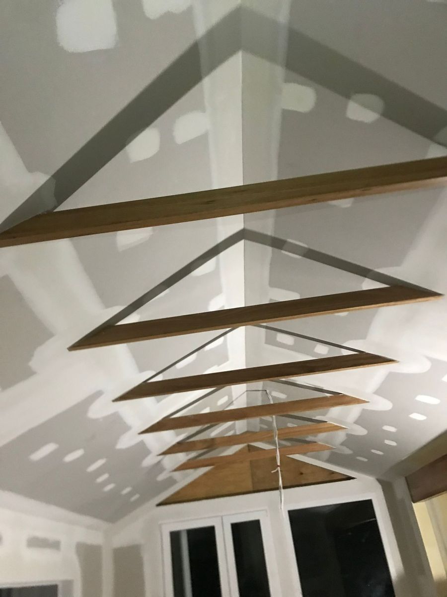 The same raked cathedral ceiling after setting, with joints taped and topped and screw heads spotted so the ceiling reads as one continuous surface between the timber beams