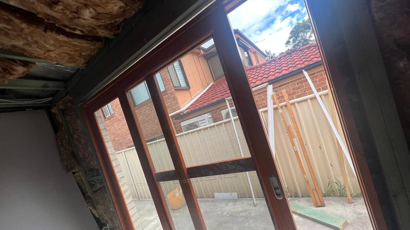 Ceiling lining pulled away from the frame above a set of glazed doors, with the insulation above exposed