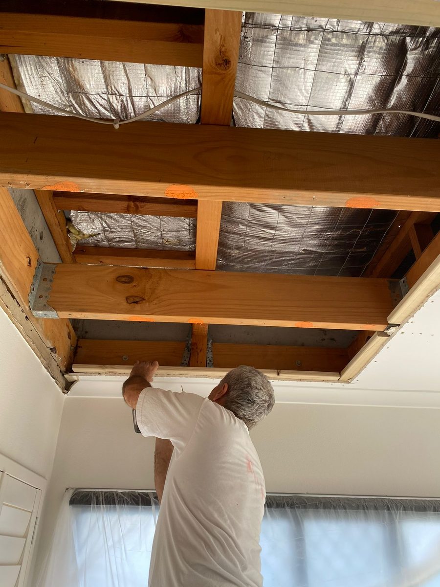 Ceiling opened to the joists below foil sarking, with someone reaching up into the opening