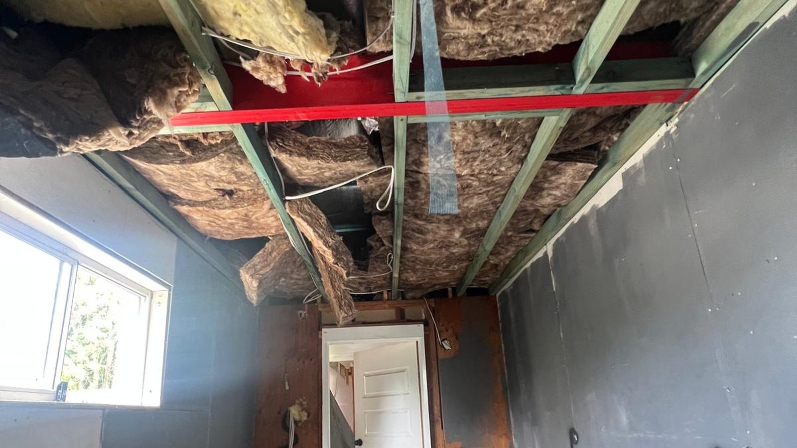 Ceiling opened back to the joists with the old insulation exposed and a steel beam above the wall line