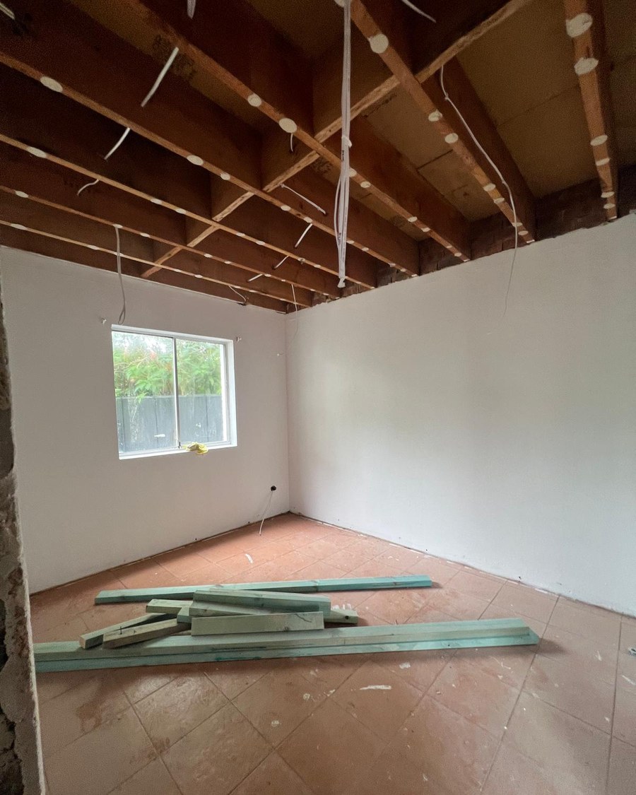 Room in a Sydney house with the failed ceiling sheets stripped out and the timber joists and wiring exposed, the walls left intact and new steel battens stacked on the floor ready for re-sheeting