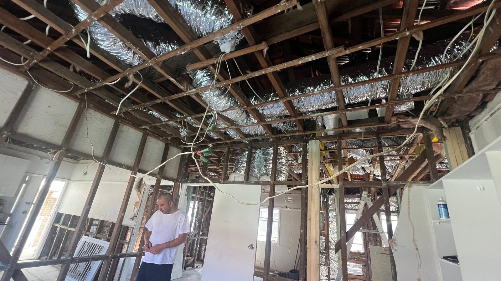 Ceiling stripped back to the framing with ducting and cabling exposed while the room is gutted