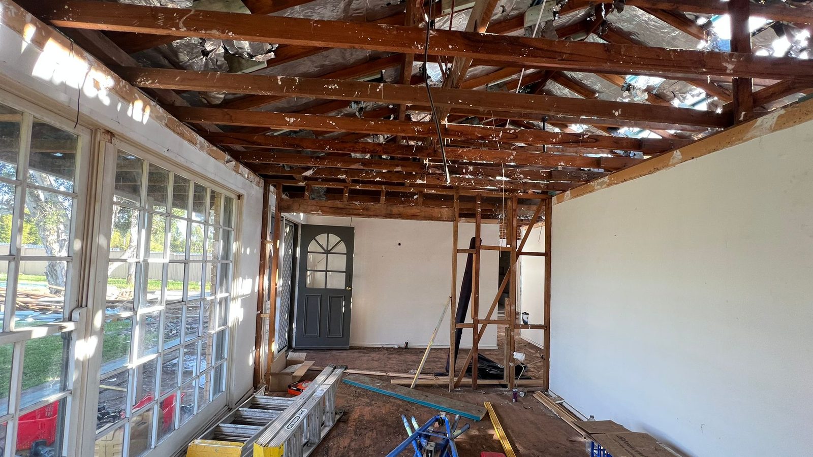 Room with the ceiling stripped back to the rafters and the floor lifted while the damage is made good