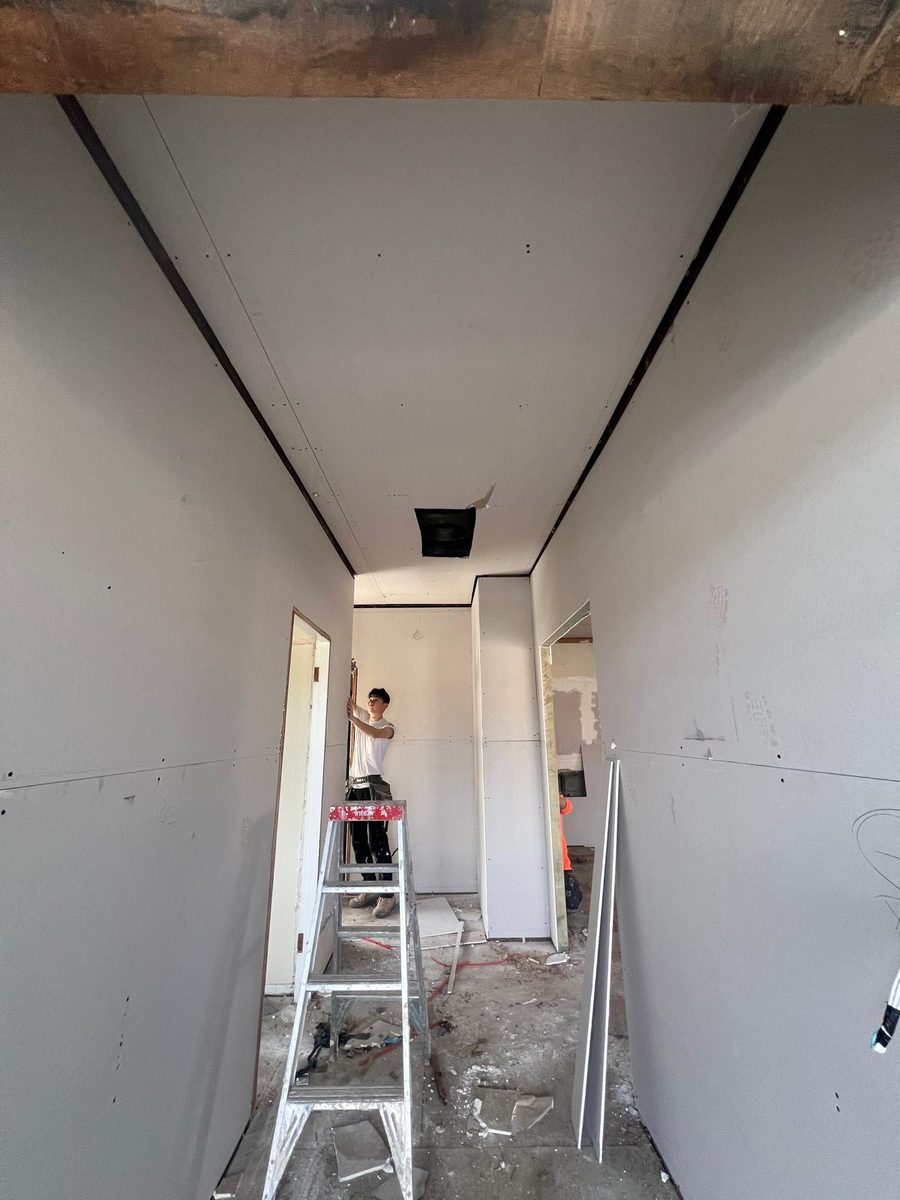 Corridor being sheeted and set, with a plasterer working from a ladder at the far end