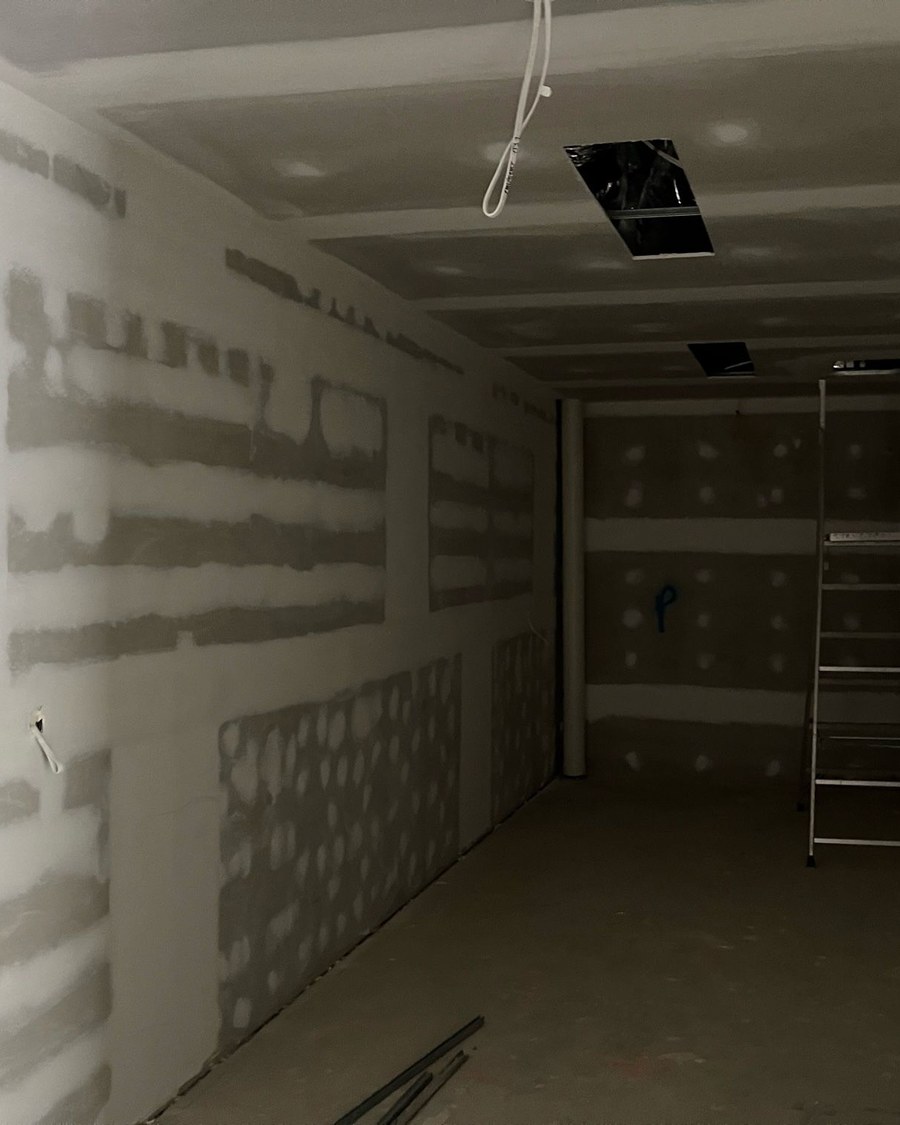 Corridor in a Sydney fit-out with the walls and ceiling sheeted in plasterboard, every joint taped and topped and each screw fixing spotted, waiting for a final sand