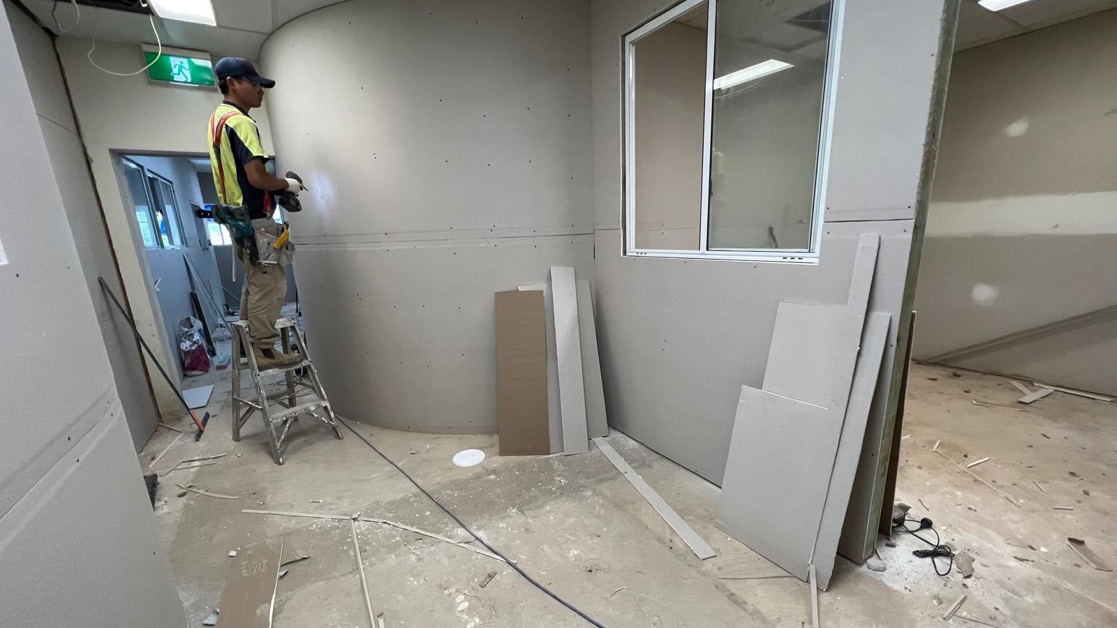 Curved wall being sheeted in an office fit out, with sheets stacked against the wall behind