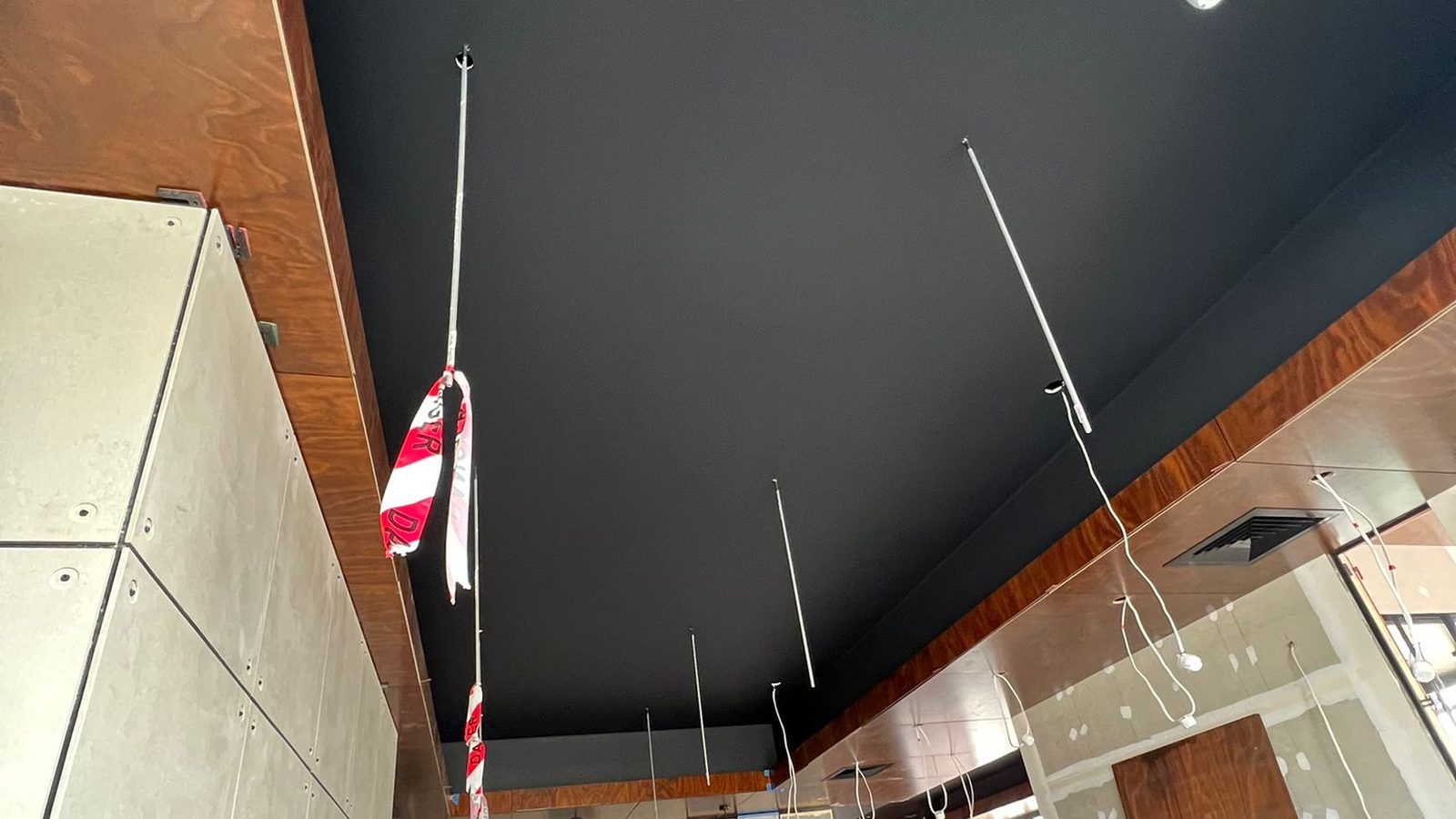 Ceiling set and finished dark against a timber lined edge, with the suspension rods and services above the fit out