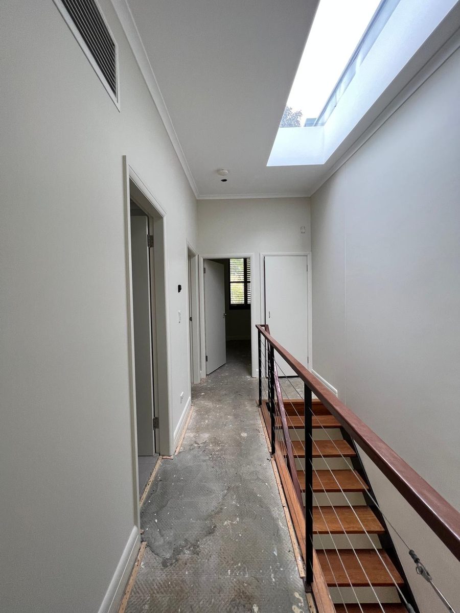 Hallway with the ceiling set around a skylight and a return air vent, the walls finished either side