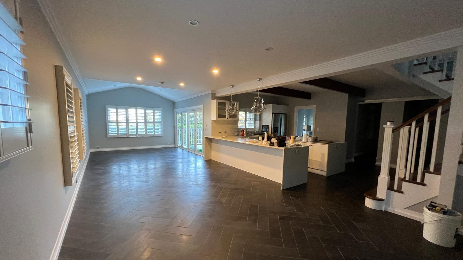 Open plan living room with a raked ceiling set flush into the cornice, downlights fitted and the kitchen beyond
