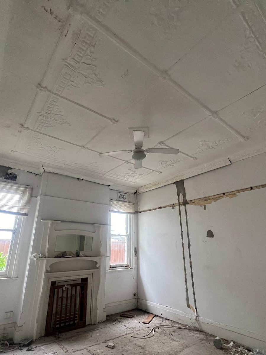 Original patterned ceiling and deep cornice in an older room, with the wall below opened up and the linings damaged