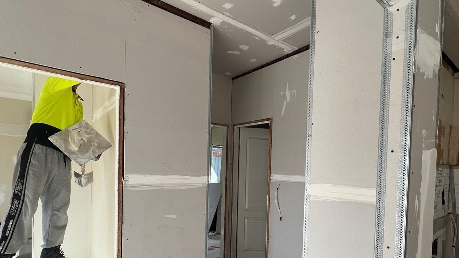 Plasterer in high visibility gear working a corner by hand in a room that has been sheeted and taped