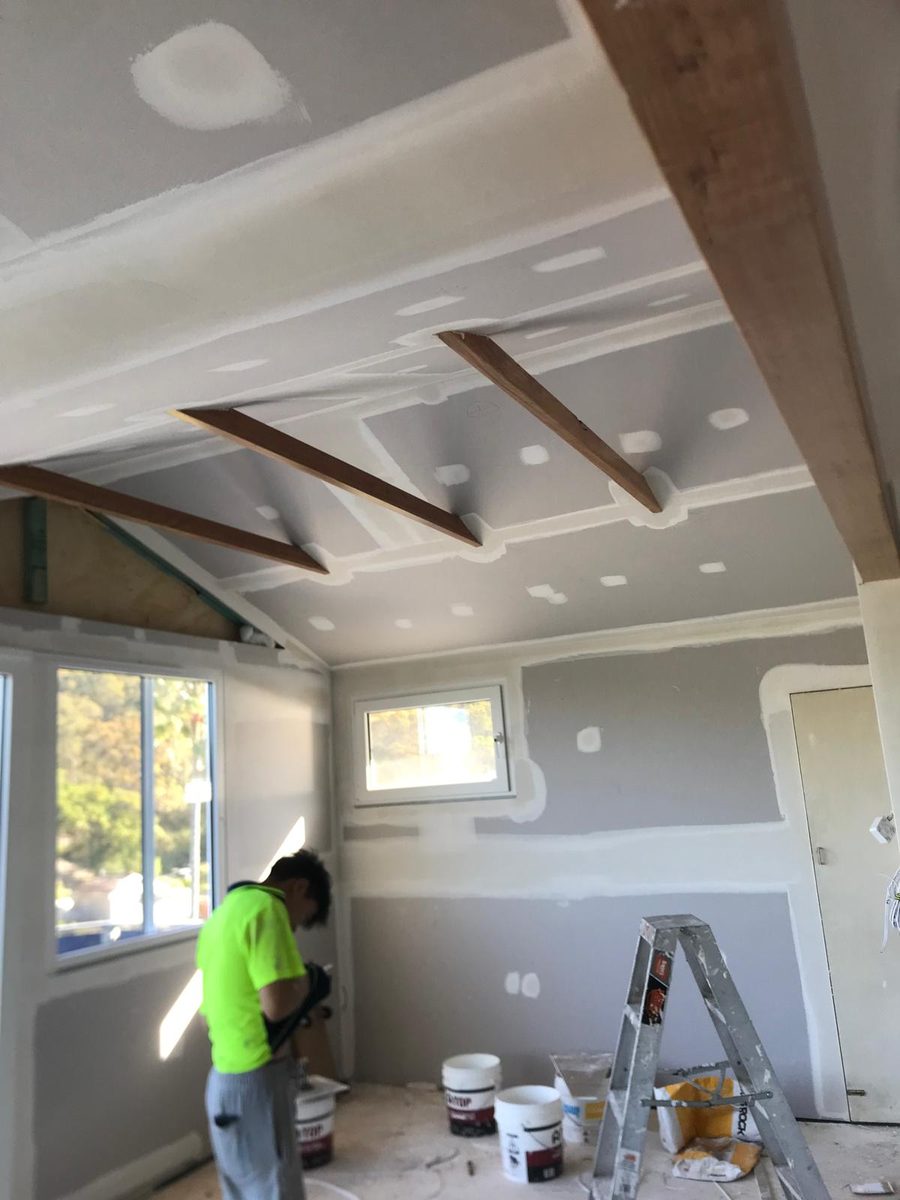 Raked ceiling with exposed beams being finished, with someone sanding the wall below