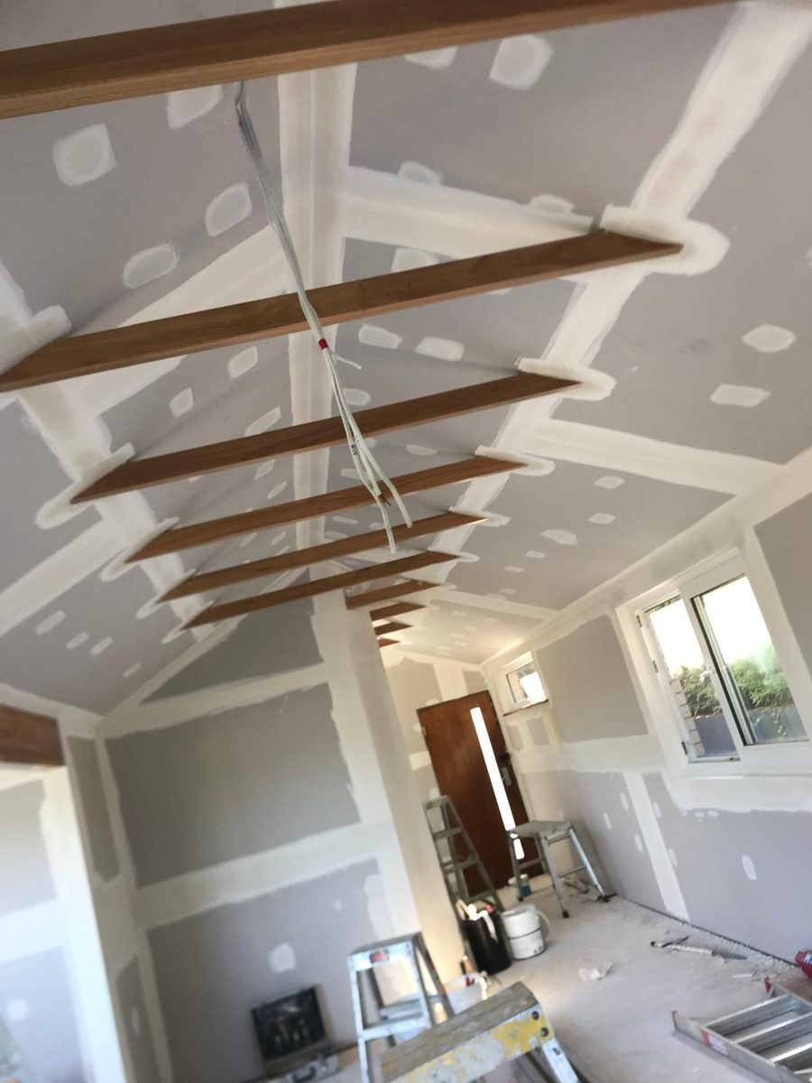 Raked ceiling coated between exposed timber beams, the joints spread ready for sanding