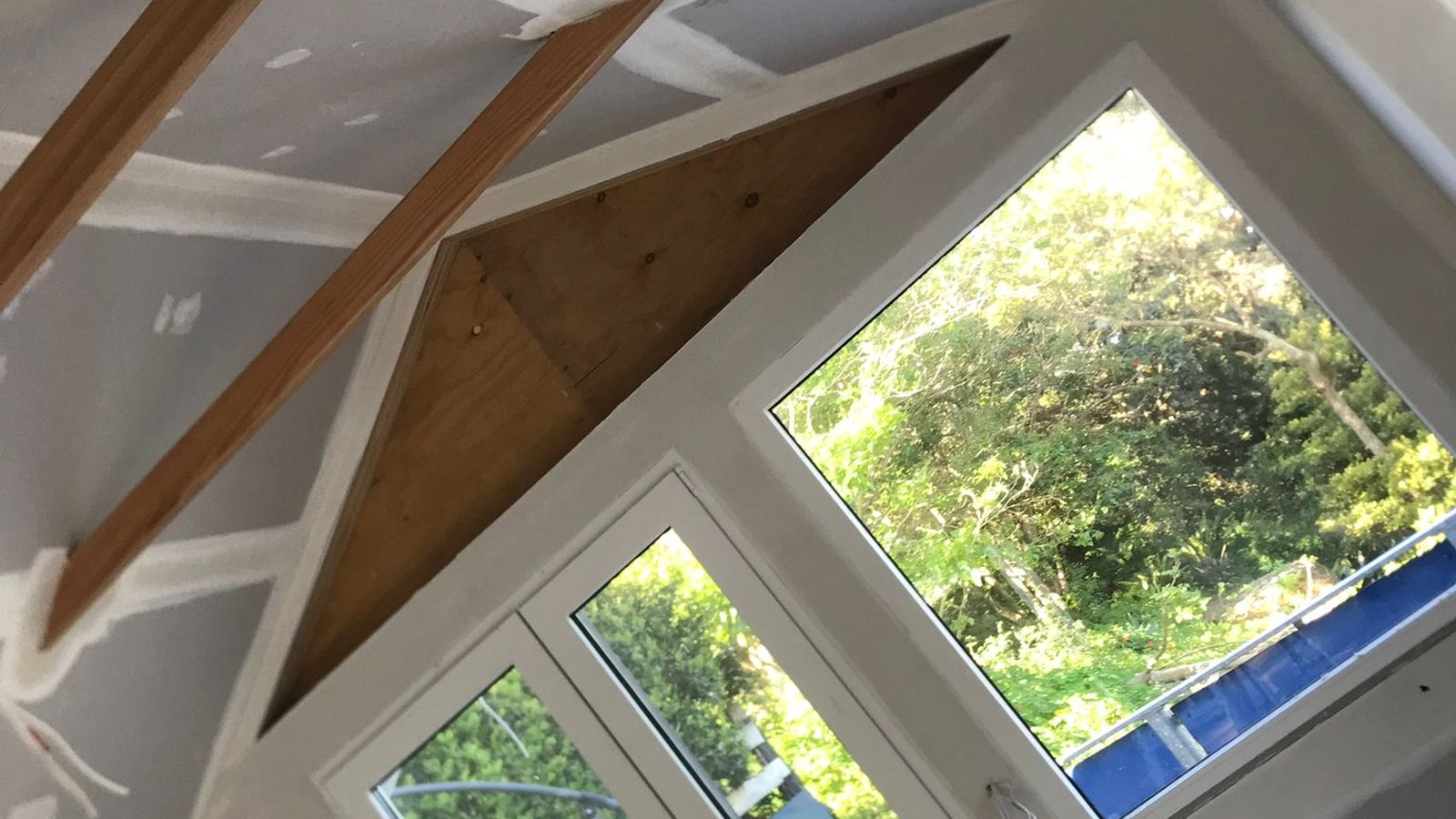 Raked ceiling set around exposed timber rafters above a run of high windows