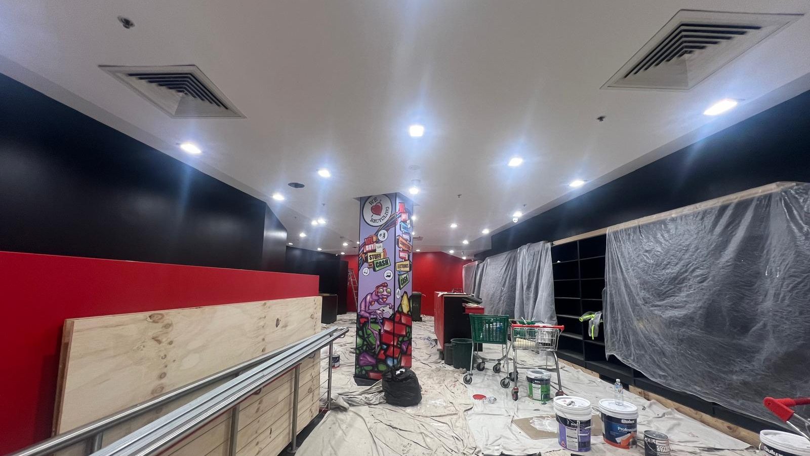 Retail fit out with the ceiling and walls finished above new shelving and drop sheets still across the floor
