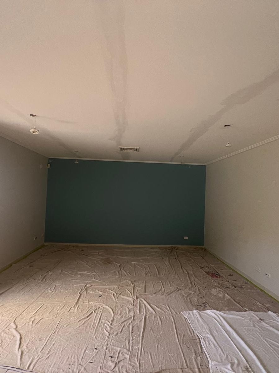 Room with the ceiling set flush above a painted wall and drop sheets across the floor
