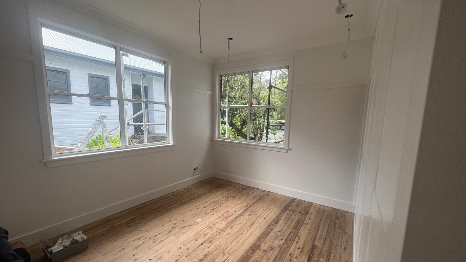 Room with the walls and ceiling set around two windows and the floorboards exposed below