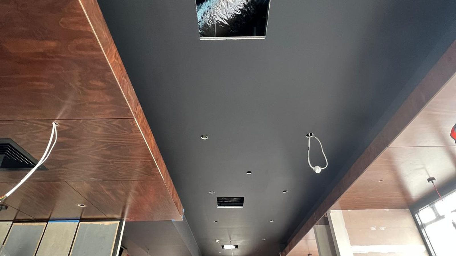 Square set ceiling meeting a timber lined soffit, with downlights and an air outlet cut in