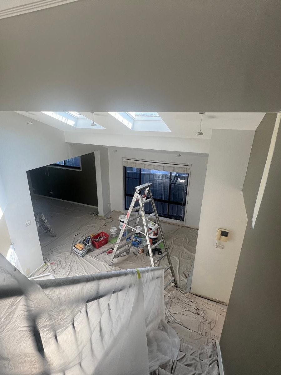 Upper level room under two skylights with drop sheets down and a ladder set up while the walls are finished