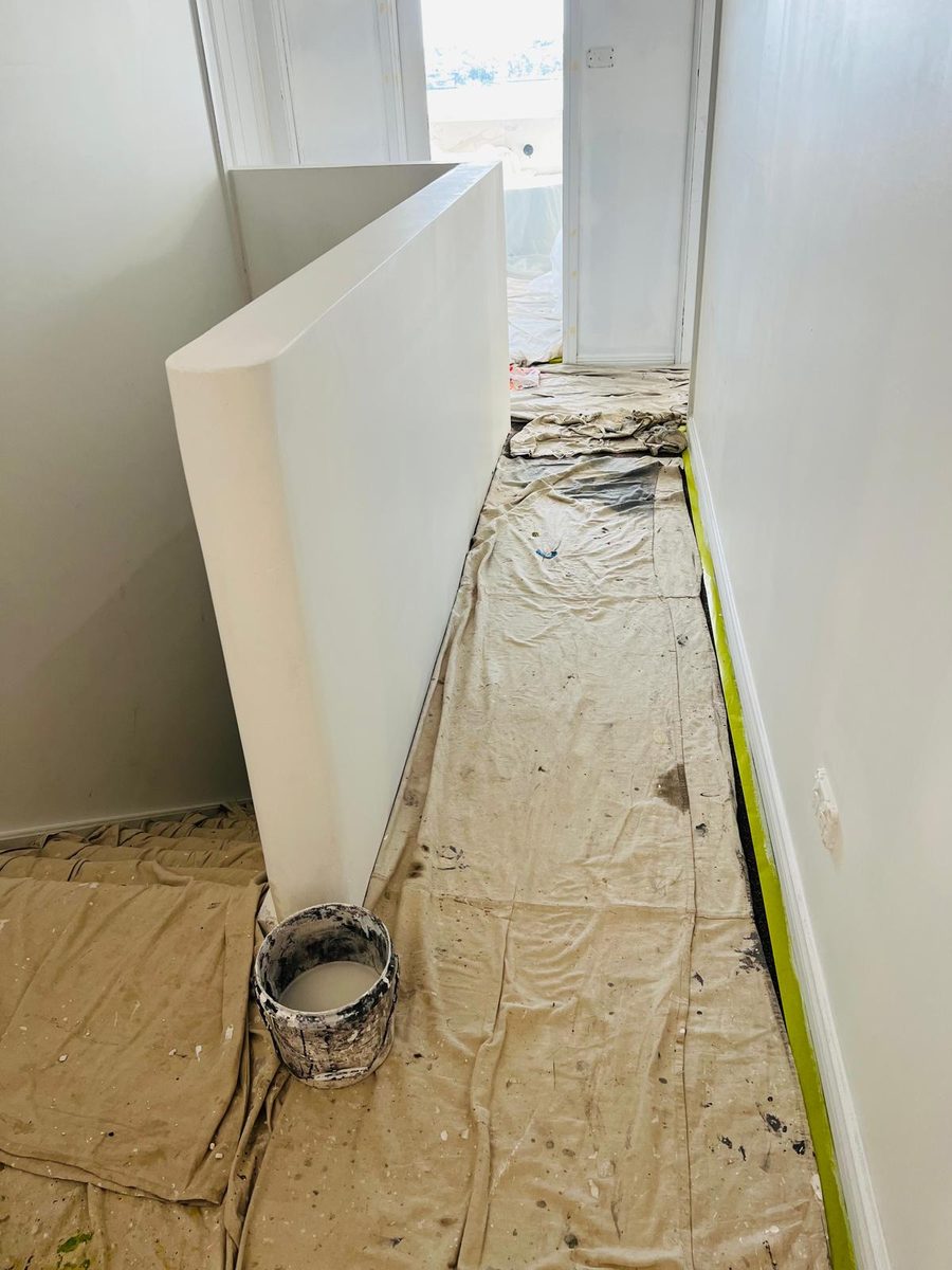 Corner of a room with the wall set and sanded, drop sheets and a compound bucket on the floor