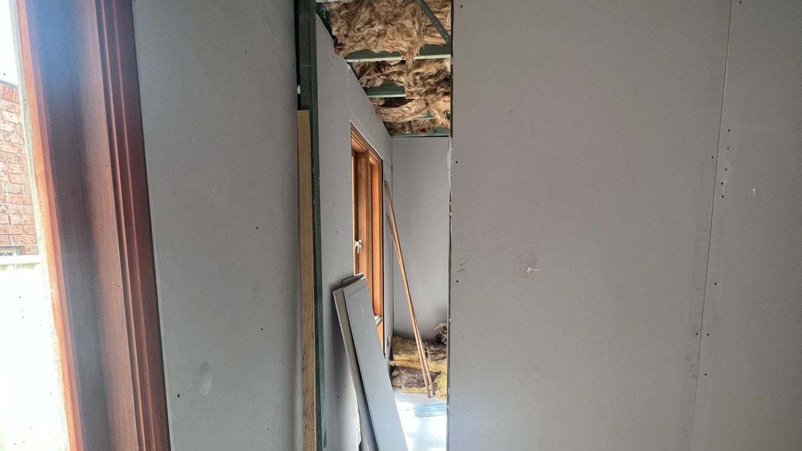 Wall sheeted in plasterboard with the ceiling still open above and insulation visible in the frame