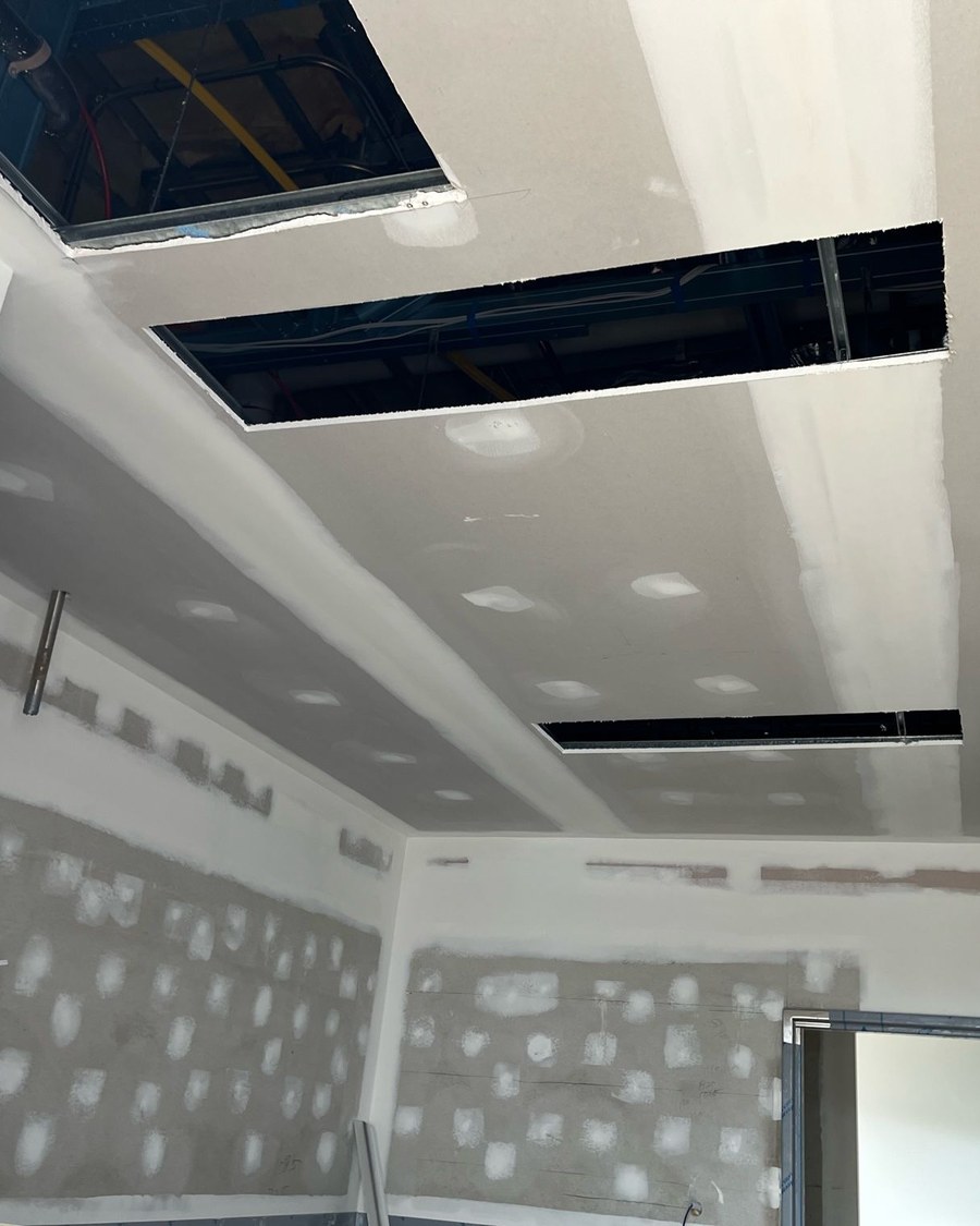 Ceiling and wall junction where every plasterboard joint has been taped and topped and each screw fixing spotted, with the service openings cut in and the surface left flat