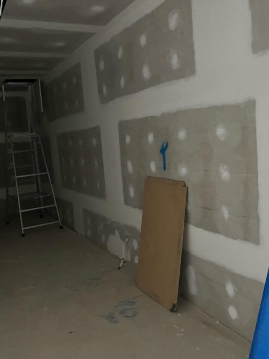 Room with the walls sheeted and every joint and screw given its first coat, a sheet offcut leaning against the wall