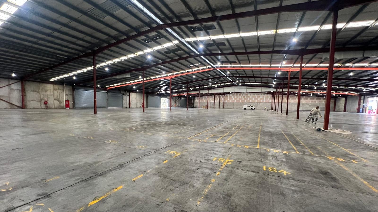 Large warehouse interior with an exposed steel roof frame and the floor marked out before fit out